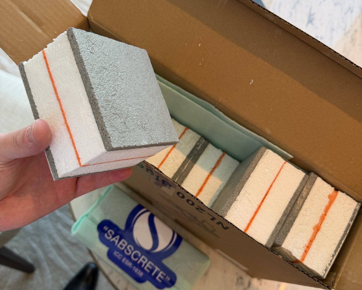 A SABS cube sample: grey SABScrete faces, white EPS foam and an orange lamination line, with more samples in a box